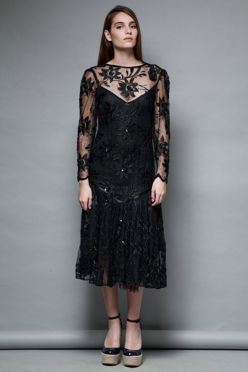 May include: A black lace dress with floral embroidery and a ruffled hem. The dress has long sleeves and a round neckline.