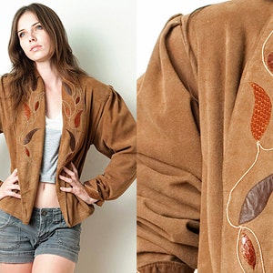 May include: A brown suede jacket with a floral design embroidered on the front and sleeves. The jacket has a shawl collar and a front zipper closure.