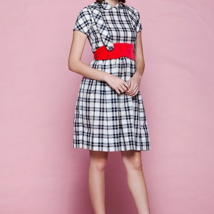 May include: A plaid dress with a red belt and red heels. The dress features a black and white checkered pattern. The red belt cinches the waist, and the red heels complete the outfit. The dress has short sleeves and a collared neckline.