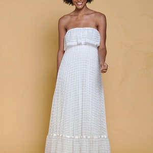 Puede incluir: Un vestido blanco maxi sin tirantes con un escote de volantes y una falda de capas. El vestido est&aacute; hecho de un delicado tejido de encaje y tiene un ajuste holgado.