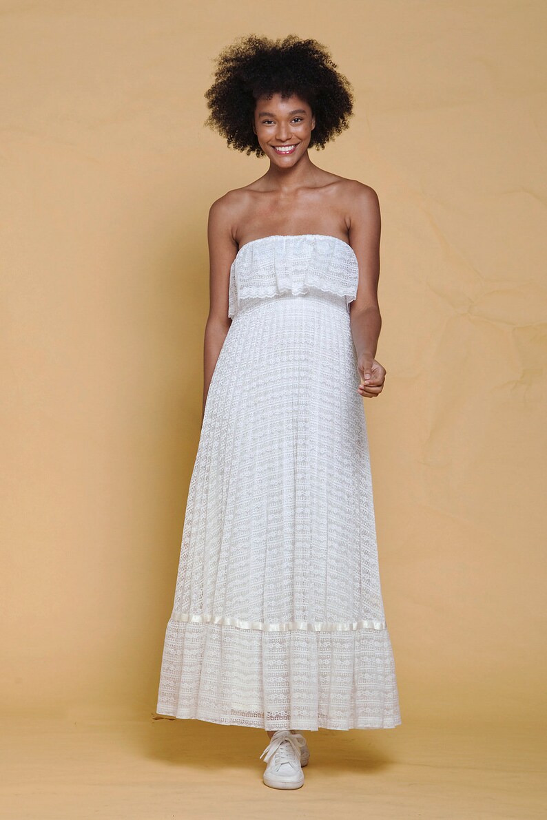 Puede incluir: Un vestido blanco maxi sin tirantes con un escote de volantes y una falda de capas. El vestido est&aacute; hecho de un delicado tejido de encaje y tiene un ajuste holgado.