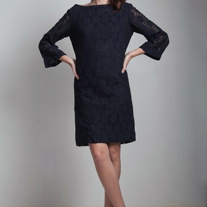May include: A black lace dress with a boat neck and 3/4 sleeves. The dress is fitted and falls to the knee. The model is wearing nude heels.