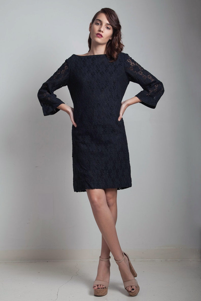 May include: A black lace dress with a boat neck and 3/4 sleeves. The dress is fitted and falls to the knee. The model is wearing nude heels.