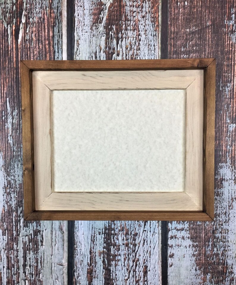 May include: A rustic wooden picture frame with a light brown inner frame and a dark brown outer frame. The frame is empty and has a white background.