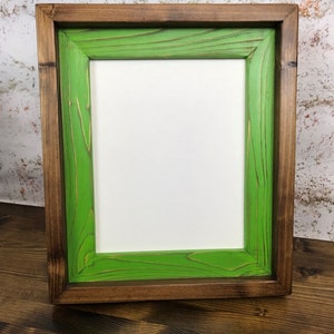 May include: A square picture frame with a dark brown outer frame and a bright green inner frame. The frame is made of wood and has a rustic look.