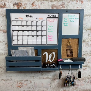 May include: A blue wooden wall organizer with a calendar, whiteboard, corkboard, and key hooks. The calendar displays the month of May 2022. The whiteboard has a grocery list and notes. Sunglasses and keys hang below.
