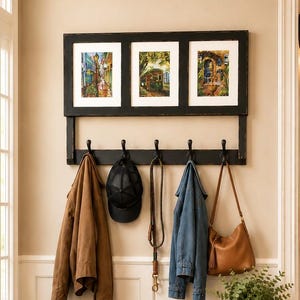 May include: A black wooden wall-mounted coat rack featuring three rectangular picture frames at the top and five black metal hooks below. Hanging from the hooks are a brown jacket, a black baseball cap, a leather leash, a blue denim jacket, and a tan leather shoulder bag.