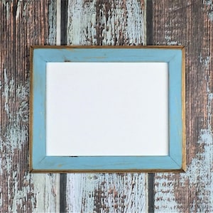 May include: A light blue picture frame with a gold trim, against a rustic wood background.