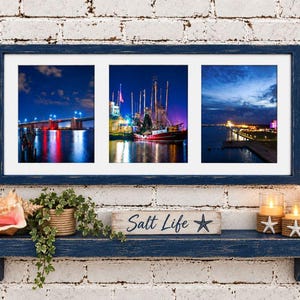 May include: A rectangular wall frame with a distressed navy blue finish containing three separate landscape photographs of a bridge, a fishing boat, and a coastal harbor at night, all illuminated by vibrant blue and warm yellow lights.