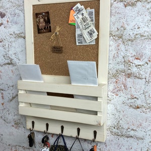 May include: White wooden wall organizer with a corkboard, mail slots, and hooks. The corkboard has a small photo, a few receipts, and a sign that says "Believe in Magic".