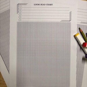 Puede incluir: Varias hojas de papel blanco "LOOM BEAD CHART" con un patr&oacute;n de cuadr&iacute;cula y l&iacute;neas punteadas. Las hojas est&aacute;n sobre una superficie de madera, con l&aacute;pices de colores y un borrador en el fondo. La cuadr&iacute;cula est&aacute; hecha de l&iacute;neas finas de color azul oscuro.