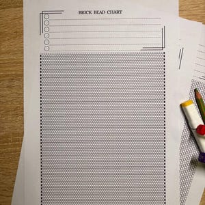 Puede incluir: Varias hojas de papel blanco con un gr&aacute;fico de cuentas de ladrillo impreso. La hoja superior tiene el texto "BRICK BEAD CHART" y una secci&oacute;n para notas. Un l&aacute;piz y marcadores son visibles. El gr&aacute;fico es una cuadr&iacute;cula de peque&ntilde;os cuadrados.