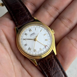 Peut inclure: Une tasse en céramique blanche avec une anse noire et le texte "But First, Coffee" dans un style manuscrit. La tasse est posée sur une surface blanche. La tasse mesure environ 10 cm de haut.