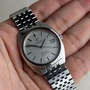 Könnte beinhalten: Eine silberfarbene Omega Constellation Automatik-Armbanduhr mit hellem Zifferblatt und Datumsfenster bei 3 Uhr. Die Uhr hat ein Edelstahlarmband. Das Zifferblatt zeigt das Omega-Logo und die Worte "Constellation Automatic".