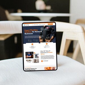 Op de afbeelding: Een digitale tablet toont een website voor een loodgietersbedrijf. De website bevat de tekst "Expert Plumbing Solutions for Homes & Businesses" en "Over 12+ Years of Experience in Plumber Service". De tablet ligt op een witte stoel.