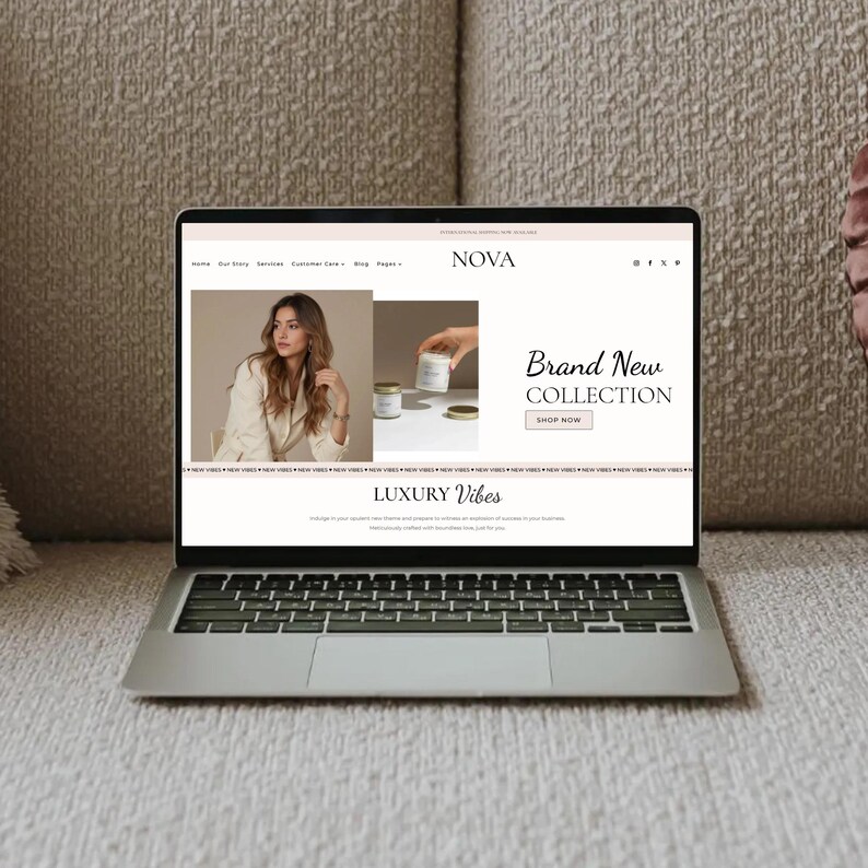 May include: A silver laptop displaying a website with the word "NOVA" at the top. The website features a woman in a cream-colored blazer, candles, and the text "Brand New Collection" and "Luxury Vibes". The laptop is on a beige couch.