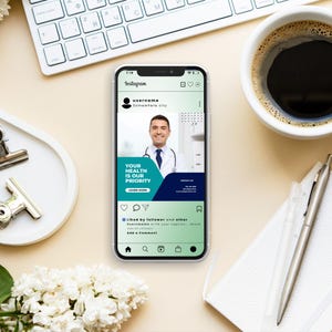 May include: A smartphone displays an Instagram post with a doctor's image and the text "YOUR HEALTH IS OUR PRIORITY". The phone is on a desk with a keyboard, coffee cup, pen, and flowers.