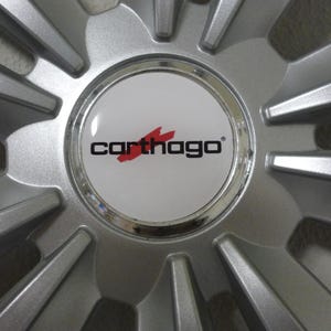Könnte beinhalten: Nahaufnahme einer silbernen Autoradfelge mit einer zentralen Nabe mit dem Logo "Carthago" in schwarzem Text mit roter Akzentuierung. Die Felge hat ein Sternmuster mit mehreren nach außen gerichteten Speichen.