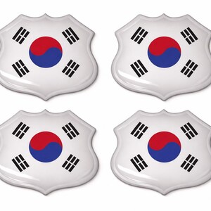 Op de afbeelding: Vier witte schildvormige stickers met de Zuid-Koreaanse vlag. Elke sticker heeft een rode cirkel met een blauw yin-yang symbool, omringd door vier zwarte trigrammen.
