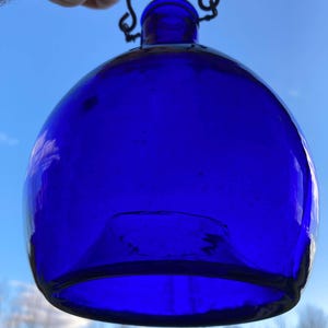 May include: A cobalt blue glass bottle with a metal hanging loop. The bottle is round and has a wide opening.