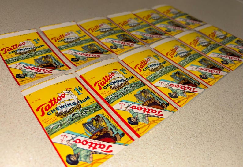 May include: A collection of vintage Tattoo Chewing Gum wrappers. The wrappers are yellow with red and blue text and illustrations of a ship, sailor, and anchor. The text includes "Tattoo Chewing Gum" and "1&cent;".