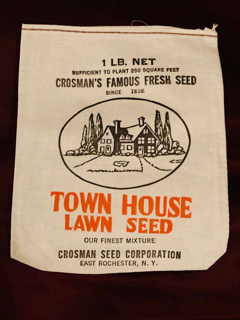May include: A white paper bag with black and orange text. The bag is for Town House Lawn Seed, a product of Crosman Seed Corporation, East Rochester, NY. The bag says "1 lb. net" and "Sufficient to plant 250 square feet". It also says "Crosman's Famous Fresh Seed since 1838". The bag has a black and white illustration of a house with trees and a small pond.