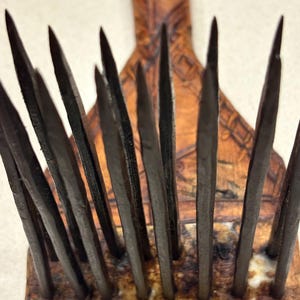 Puede incluir: Primer plano de una herramienta de madera con m&uacute;ltiples p&uacute;as de metal oscuro. Las p&uacute;as est&aacute;n dispuestas en fila y son afiladas. El mango es de madera y tiene un dise&ntilde;o tallado. La herramienta parece ser vintage o antigua.