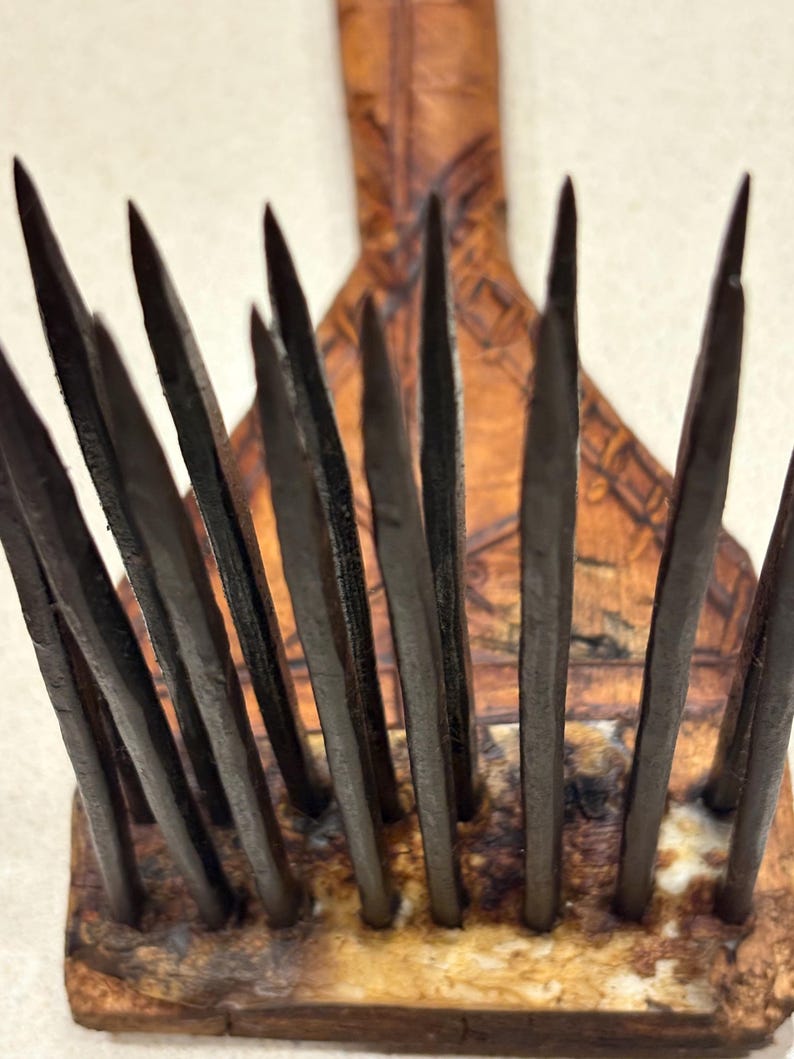 Puede incluir: Primer plano de una herramienta de madera con m&uacute;ltiples p&uacute;as de metal oscuro. Las p&uacute;as est&aacute;n dispuestas en fila y son afiladas. El mango es de madera y tiene un dise&ntilde;o tallado. La herramienta parece ser vintage o antigua.