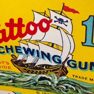 May include: Vintage Tattoo Chewing Gum advertisement. The yellow background features a pirate ship with white sails and a skull and crossbones flag. The text includes "Tattoo" in red, "Chewing Gum" in blue, and a price of 1&cent;.