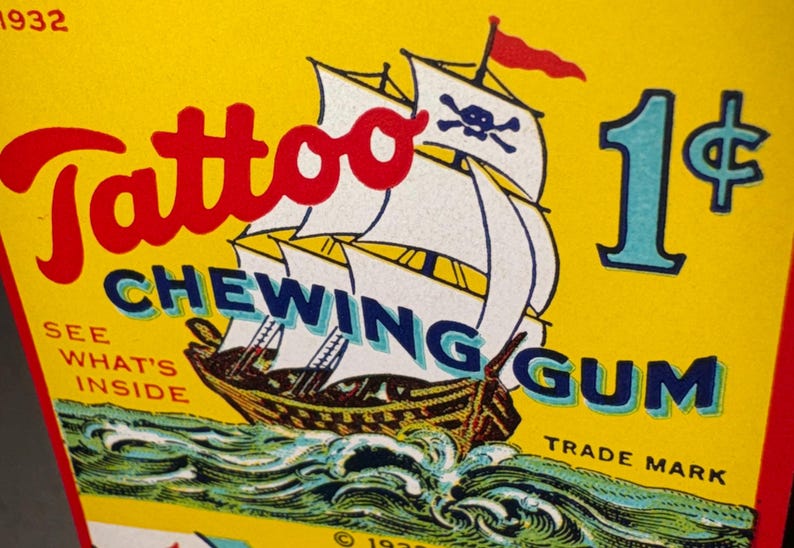 May include: Vintage Tattoo Chewing Gum advertisement. The yellow background features a pirate ship with white sails and a skull and crossbones flag. The text includes "Tattoo" in red, "Chewing Gum" in blue, and a price of 1&cent;.