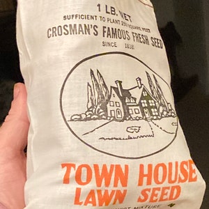 May include: A white burlap bag with black and orange text that reads "Crosman's Famous Fresh Seed" and "Town House Lawn Seed". The bag is 1 lb. net and is sufficient to plant 250 square feet. The bag also features a black and white illustration of a house with trees and a driveway.