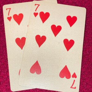 Puede incluir: Se muestran dos cartas de juego, ambas el siete de corazones. Las cartas tienen un fondo blanco con s&iacute;mbolos de coraz&oacute;n rojos y el n&uacute;mero siete en las esquinas. Las cartas parecen ligeramente desgastadas.