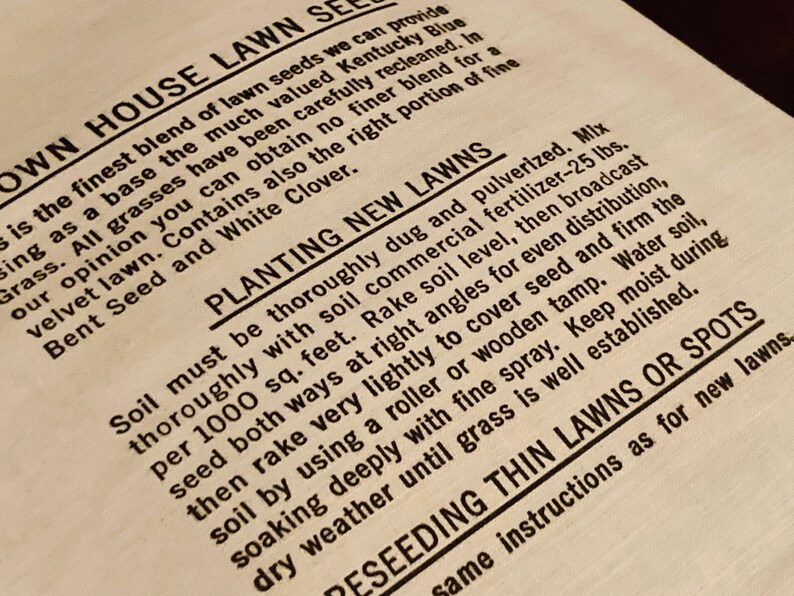 May include: Close-up of a vintage lawn seed packet with instructions for planting new lawns. The text reads "Own House Lawn Seeds" and includes information about the blend of seeds, including Kentucky Blue Grass, Bent Seed, and White Clover.