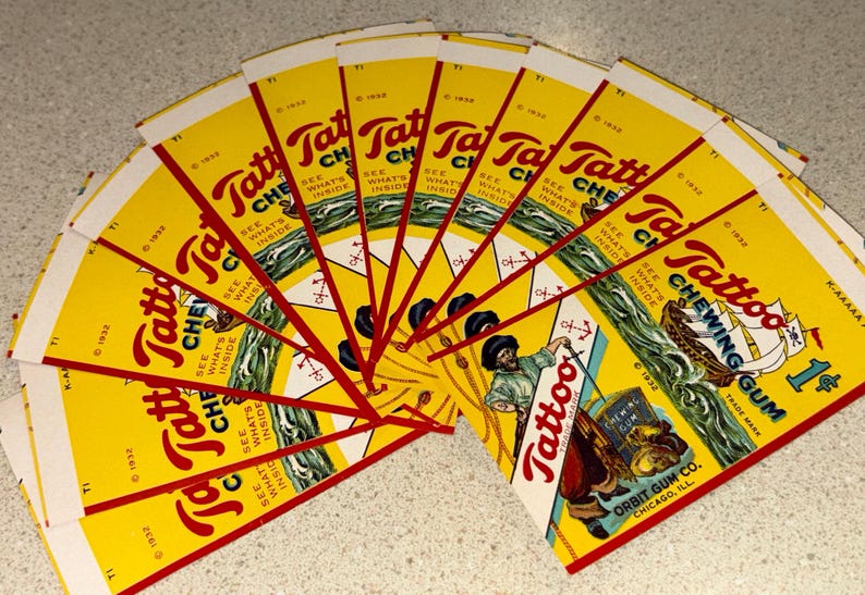 May include: A fan of vintage Tattoo Chewing Gum wrappers. The wrappers are yellow with red and white text and graphics. The wrappers feature a sailor and a ship. The wrappers are from 1932.