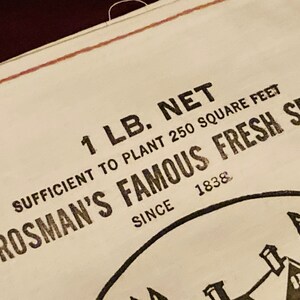 May include: A white paper bag with black text that reads "1 LB. NET SUFFICIENT TO PLANT 250 SQUARE FEET CROSMAN'S FAMOUS FRESH SEED SINCE 1838".