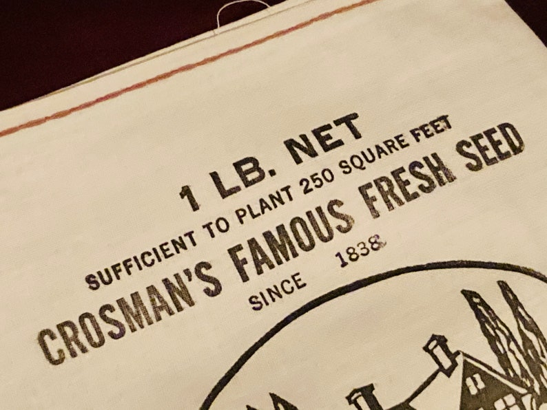 May include: A white paper bag with black text that reads "1 LB. NET SUFFICIENT TO PLANT 250 SQUARE FEET CROSMAN'S FAMOUS FRESH SEED SINCE 1838".