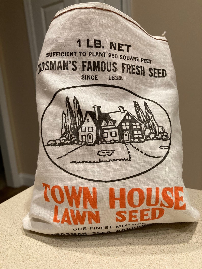 May include: A white burlap bag with black and orange text that reads "1 LB. NET", "SUFFICIENT TO PLANT 250 SQUARE FEET", "CROSMAN'S FAMOUS FRESH SEED", "SINCE 1838", "TOWN HOUSE", "LAWN SEED", "OUR FINEST MIXTURE", and "CROSMAN SEED CORP.". The bag features a black and white illustration of a house with a lawn.