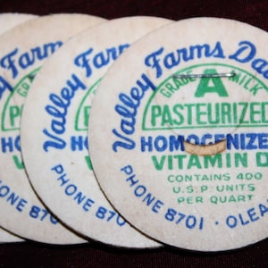 May include: Four white milk bottle caps with blue and green text that reads "Valley Farms Dairy, Inc."  The text also says "Grade A Pasteurized Homogenized Vitamin D" and "Contains 400 U.S.P. Units Per Quart" and "OLEAN, N.Y."