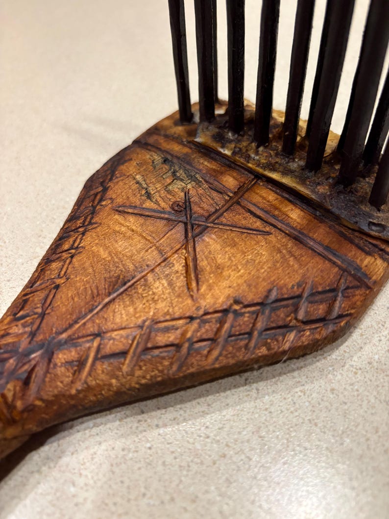 Puede incluir: Primer plano de un peine de madera con acabado marr&oacute;n oscuro. El peine presenta un dise&ntilde;o tallado con una cruz y patrones geom&eacute;tricos. Los dientes del peine son oscuros y est&aacute;n espaciados uniformemente.