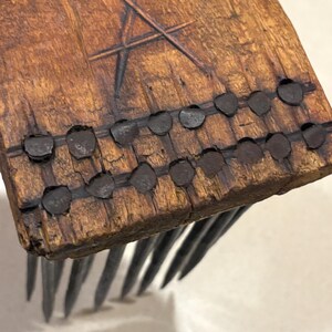 Puede incluir: Primer plano de un peine de madera hecho a mano con p&uacute;as de metal. El mango de madera del peine es de color marr&oacute;n oscuro con un dise&ntilde;o de estrella tallada y remaches met&aacute;licos. Las p&uacute;as met&aacute;licas son largas y espaciadas uniformemente.