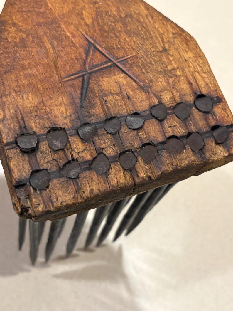 Puede incluir: Primer plano de un peine de madera hecho a mano con p&uacute;as de metal. El mango de madera del peine es de color marr&oacute;n oscuro con un dise&ntilde;o de estrella tallada y remaches met&aacute;licos. Las p&uacute;as met&aacute;licas son largas y espaciadas uniformemente.