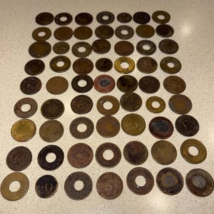 May include: A collection of numerous circular metal washers and vintage coins arranged in a grid pattern. The items vary in size, color, and texture, featuring weathered brown, bronze, and metallic tones with some pieces containing center holes.