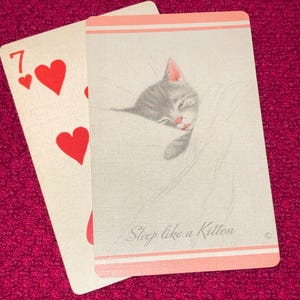 Puede incluir: Dos cartas de juego sobre un fondo rosa. Una carta muestra el n&uacute;mero siete y tres corazones rojos. La otra carta presenta un gatito gris durmiendo con el texto "Sleep like a Kitten" en un borde rosa claro.
