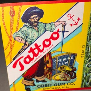 May include: Vintage "Tattoo" chewing gum box featuring a pirate illustration. The pirate holds a sword and stands next to a treasure chest. The box has a yellow background with red and blue accents. The text "Orbit Gum Co. Chicago, Ill." is visible.