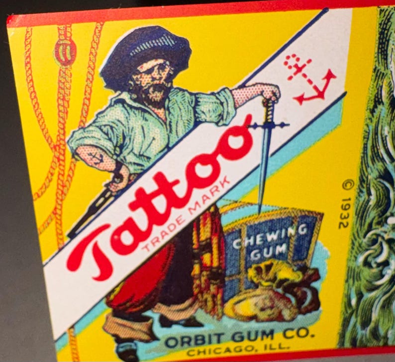 May include: Vintage "Tattoo" chewing gum box featuring a pirate illustration. The pirate holds a sword and stands next to a treasure chest. The box has a yellow background with red and blue accents. The text "Orbit Gum Co. Chicago, Ill." is visible.