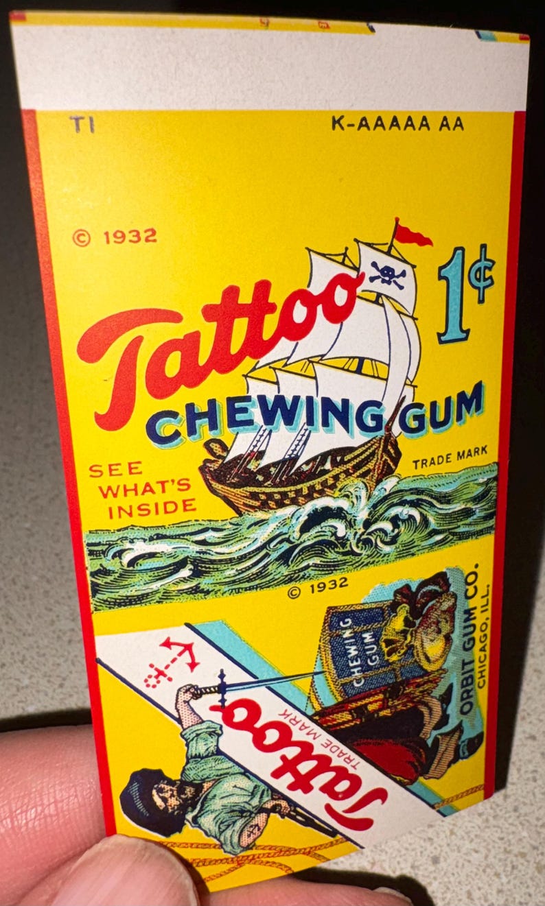 May include: Vintage Tattoo Chewing Gum package from 1932. The yellow package features a pirate ship with a skull and crossbones flag, waves, and the text "Tattoo Chewing Gum." The price is 1&cent;.