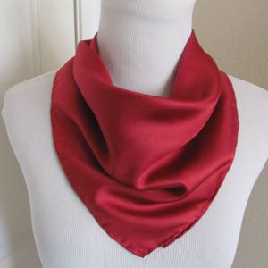 May include: A red silk scarf on a white mannequin. The scarf is folded in a triangle shape and draped around the mannequin's neck.
