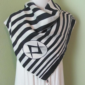 May include: A black and white striped scarf with a geometric design in an oval. The scarf is draped over a white mannequin. The scarf has diagonal stripes and a white border.