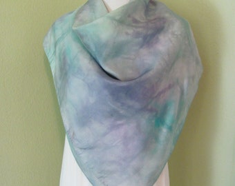 May include: A light blue, green, and purple silk scarf with a tie-dye pattern. The scarf is draped over a white mannequin.