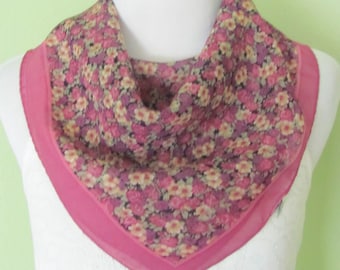May include: A pink floral patterned silk scarf with a pink border. The scarf is folded and displayed on a white mannequin.